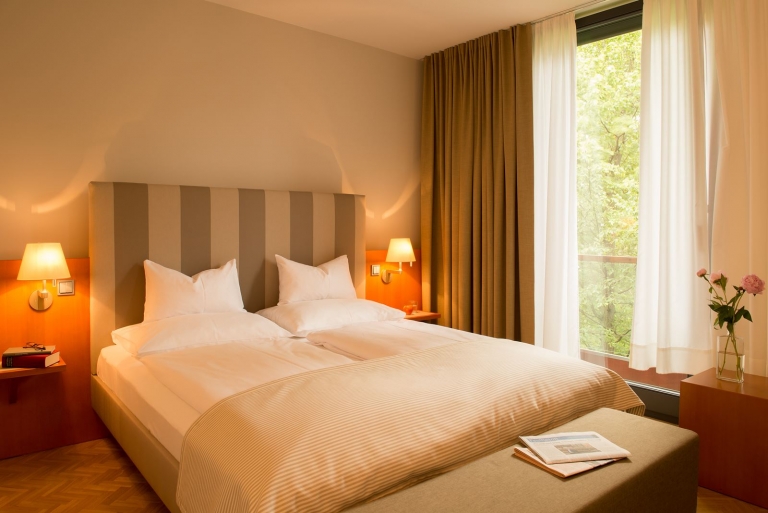 Superior Zimmer mit Blick auf das große Doppelbett mit erleuchteten Wandlampen und Blick auf das Grün der anliegenden Bäume