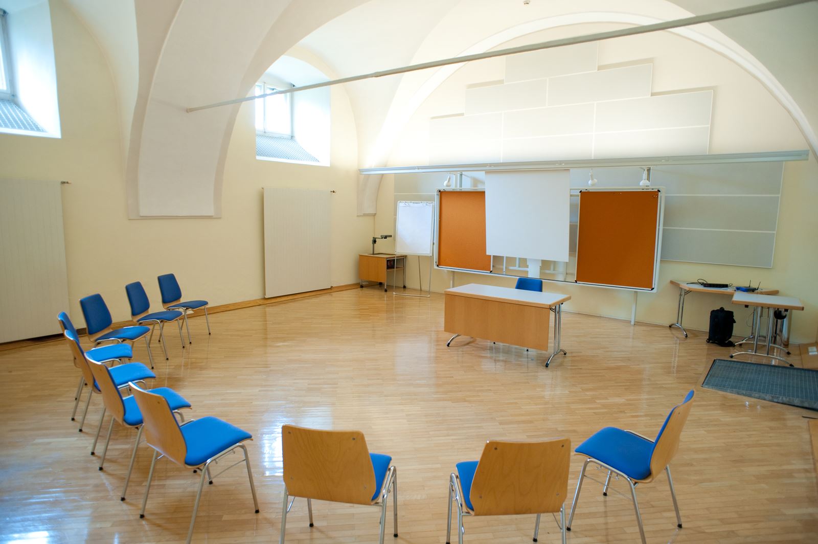 Seminarraum2 mit Sessel Halbkreis, Pinwand und Leinwand. Licht strahlt durch die Oberfenster