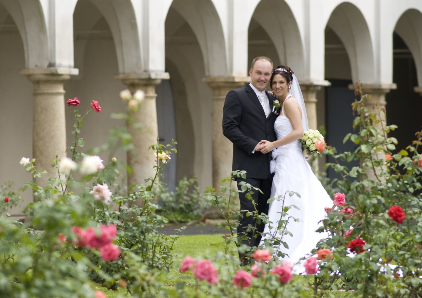 Ein Brautpaar steht umschlungen vor dem Oberschloss. Im Vordergrund zartrosa und rot blühende Rosen