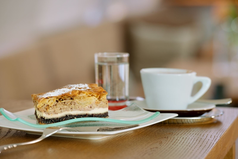 Ein leckeres Stück Kuchen und eine Tasse Kaffee mit einem Glas Wasser stehen auf einem Holztisch