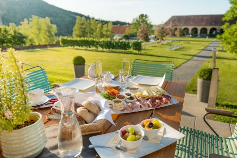 Ein Frühstückstisch mit verschiedenen Köstlichkeiten ist auf der Schlossterrasse aufgedeckt. Im Hintergrund die grünen Wiesen und das Pool der Schlossanlage