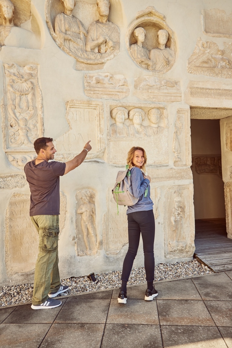 EIn Mann und eine Frau bewundern die Römersteine am Oberschloss des Schloss Seggau