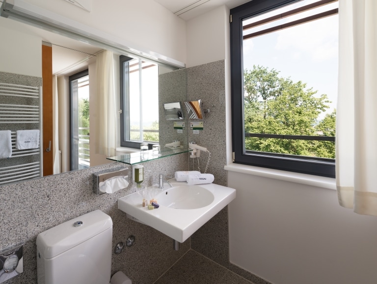 Bathroom of the modern smart double room at Schloss Seggau. A modern white sink, hairdryer, mirrow and a great view of the green surrounding